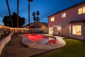 A swimming pool with a curved design, surrounded by a landscaped area with palm trees and a patio with outdoor furniture.