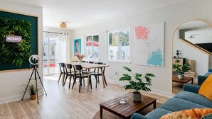 A modern living room with a wooden floor, a blue sofa, a coffee table, and a dining area with a wooden table and chairs.