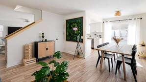 A modern living room with a wooden staircase, a dining area with a table and chairs, and a kitchen in the background.