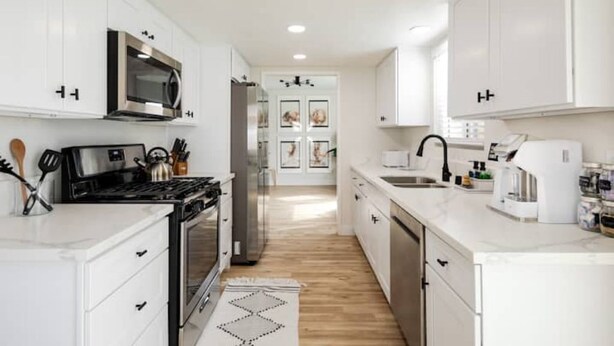 A modern kitchen with white cabinets, stainless steel appliances, and a wooden floor.