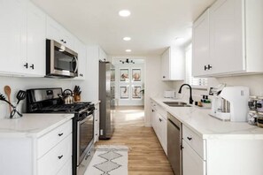 A modern kitchen with white cabinets, stainless steel appliances, and a wooden floor. - All-inclusive Dream; Big Pool, Game Room, King Bed (Indio)