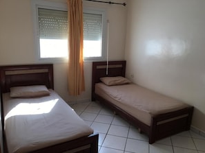 A bedroom with two single beds, a window with blinds, and a curtain.