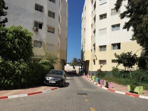 A residential street with two-story apartment buildings, a parked car, and a clear sky.