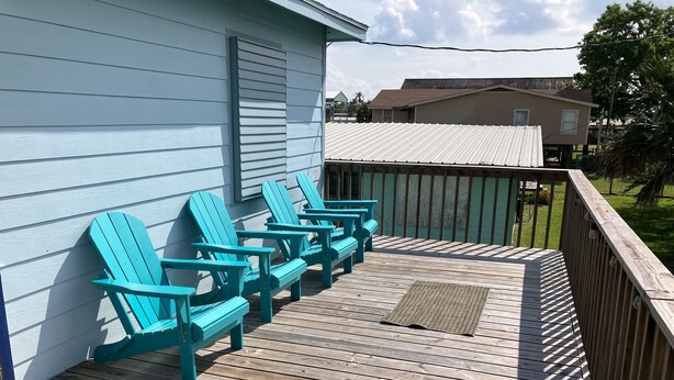 Een houten terras met turquoise Adirondack-stoelen en een houten balustrade.
