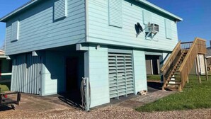Een lichtblauw huis met twee verdiepingen, een schotelantenne, een garage en een houten trap die naar de tweede etage leidt.