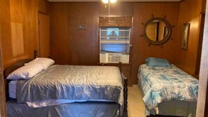 Een slaapkamer met twee bedden, een plafondventilator, een raam met zonwering en een spiegel aan de muur.