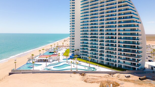 A modern hotel with a curved facade, multiple balconies, and a pool area with a water slide. - Encantame Towers (Puerto Peñasco)