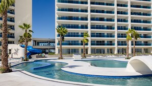 A hotel pool area with a water slide, palm trees, and a modern building with balconies. - Encantame Towers (Puerto Peñasco)