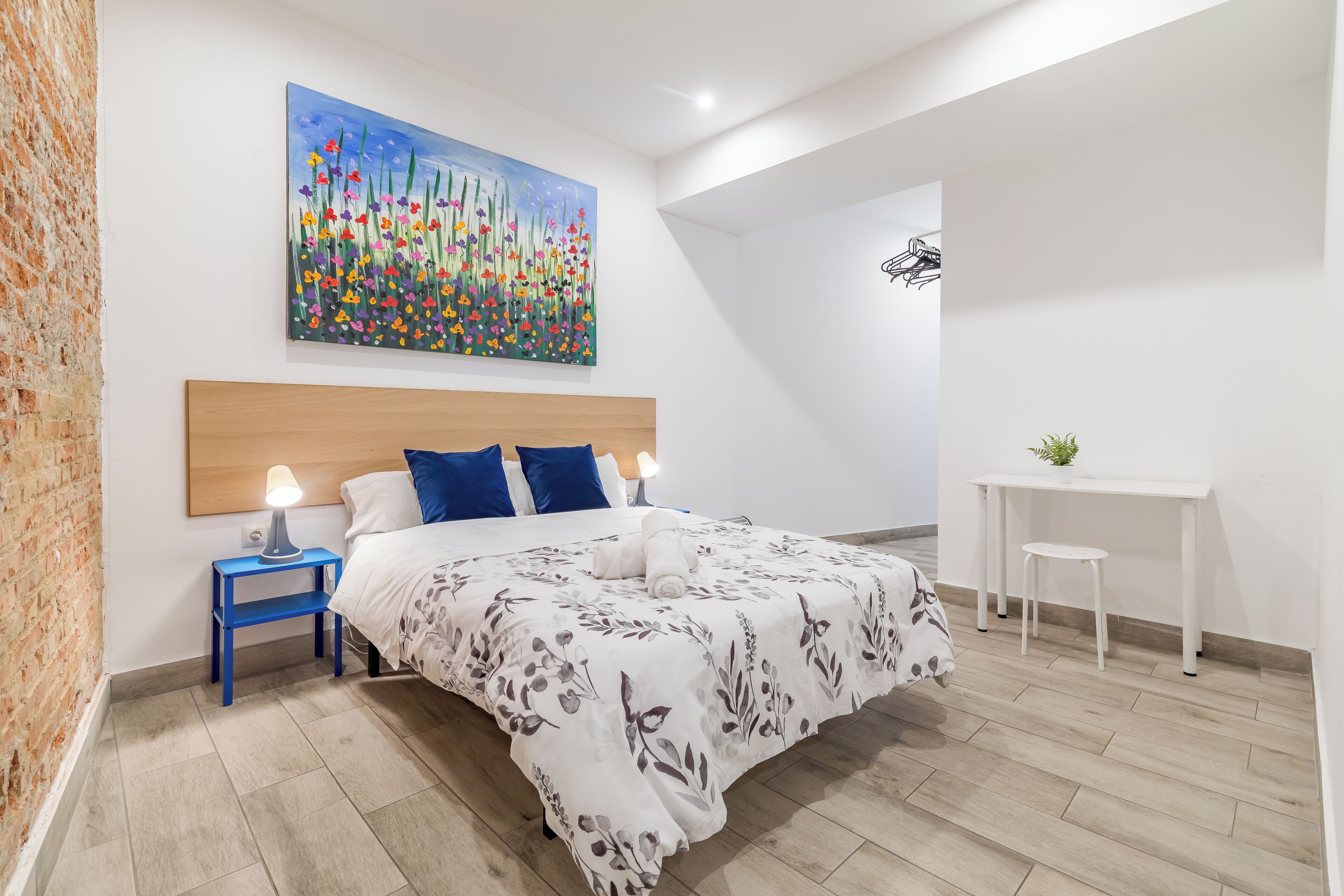 Un dormitorio con cama, mesita de noche, escritorio y un cuadro en la pared.