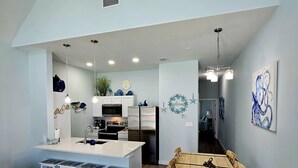 A spacious kitchen with a central island, a dining area with a wooden table and chairs, and a living area with a dark blue sofa. - Hightide Hideaway Beach Getaway. (Corpus Christi)