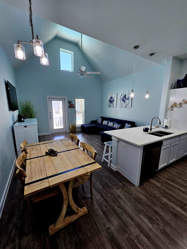 A modern kitchen with a wooden dining table, a built-in island with a sink, and a ceiling fan. - Hightide Hideaway Beach Getaway. (Corpus Christi)