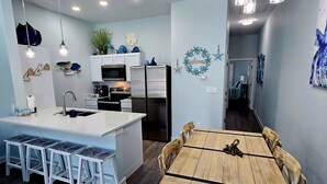 A modern kitchen with a central island, bar stools, and a dining table with chairs. - Hightide Hideaway Beach Getaway. (Corpus Christi)