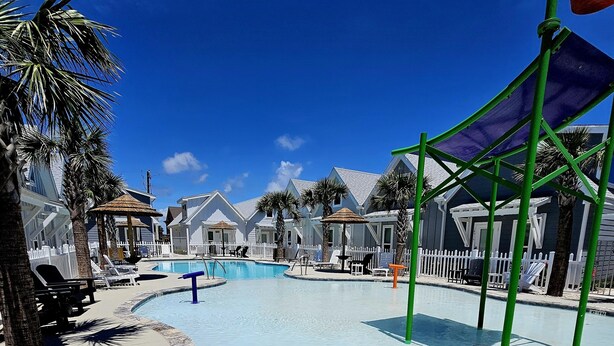 A pool area with a clear blue sky, palm trees, and a white fence. - Hightide Hideaway Beach Getaway. (Corpus Christi)