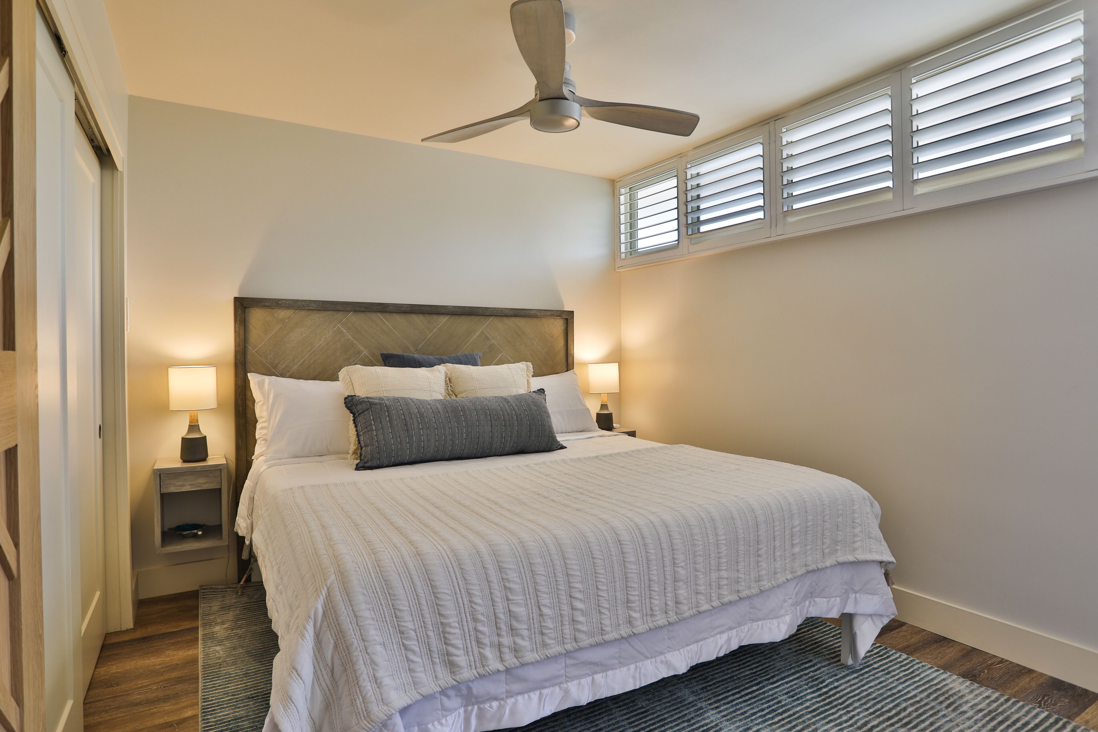 Une chambre à coucher avec un grand lit, un ventilateur de plafond, des lampes de chevet et une fenêtre avec des stores.