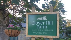 Une pancarte indiquant la ferme de Clover Hill et faisant la publicité de ses hébergements insolites et de ses chalets.