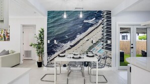 A modern kitchen with a mural of a beach scene, a dining table with chairs, and pendant lighting.