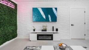 A modern living room with a large flat-screen TV mounted on a white brick wall, a white entertainment unit below, and a green wall on one side.