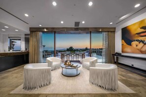Un salon moderne doté d’une grande fenêtre, d’une table basse ronde et de fauteuils à franges blanches.