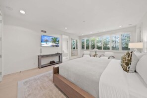 Een slaapkamer met een groot bed, een televisie, een bureau en een raam met jaloezieën.
