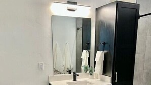 Un baño moderno con inodoro blanco, tocador negro con espejo y lavamanos blanco.