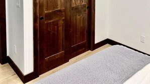 Una habitación con un armario de madera, un televisor de pantalla plana montado encima y una alfombra gris en el suelo.