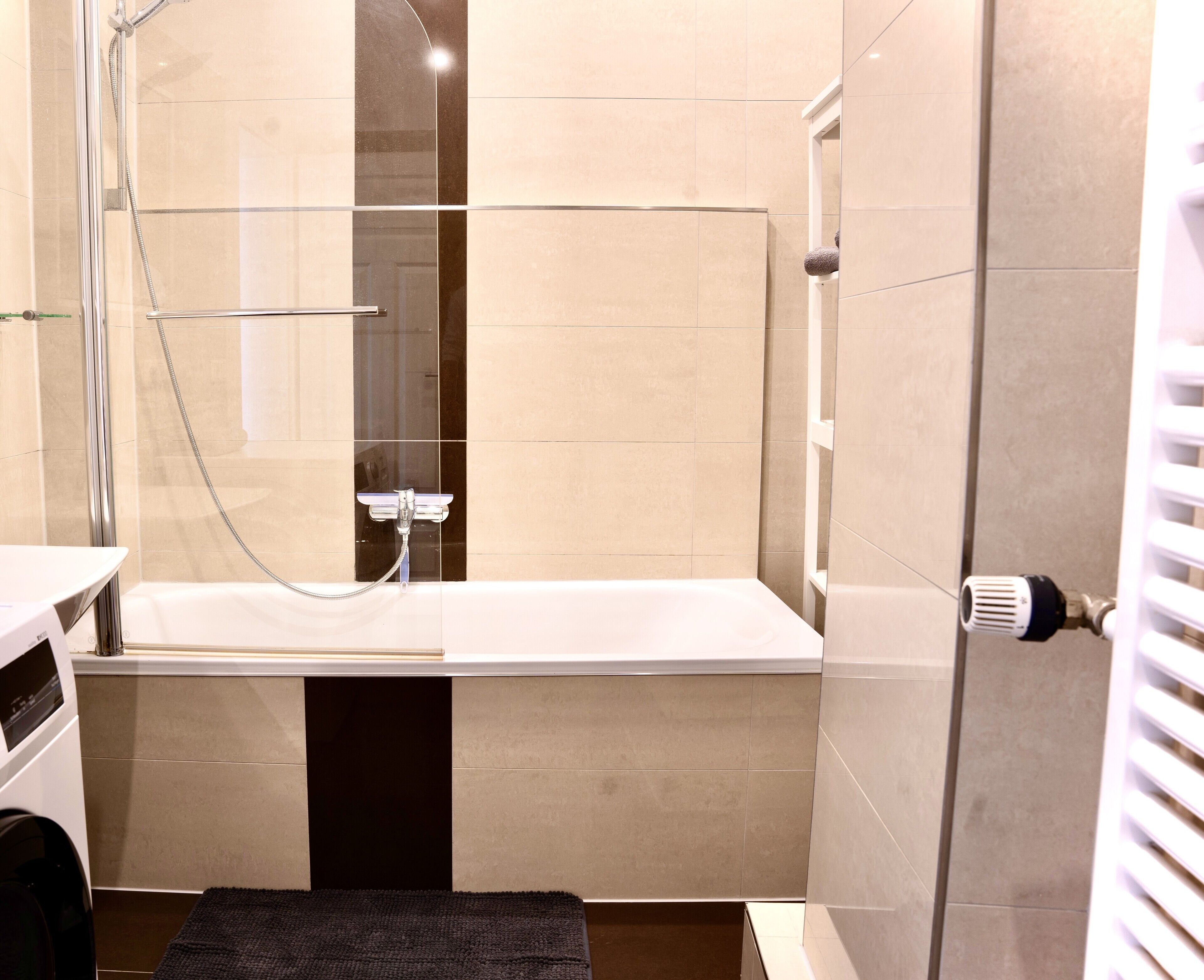 Un baño moderno con ducha envuelta en vidrio, una bañera blanca y un perchero para toallas.