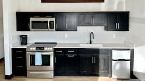 A modern kitchen with dark cabinets, stainless steel appliances, and a pendant light. - 103 Brand New Studio near Glacier Park (Columbia Falls)