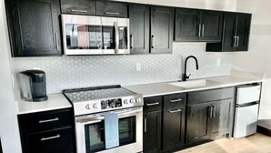 Una cocina moderna con electrodomésticos de acero inoxidable, armarios negros y encimera blanca.