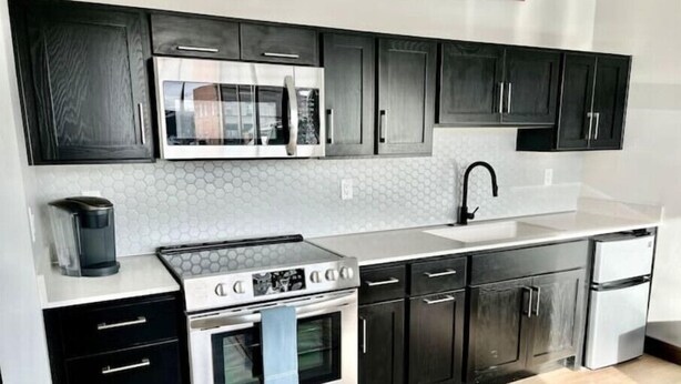A modern kitchen with stainless steel appliances, black cabinets, and a white countertop.