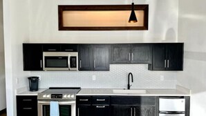 A modern kitchen with dark cabinets, stainless steel appliances, and a pendant light.