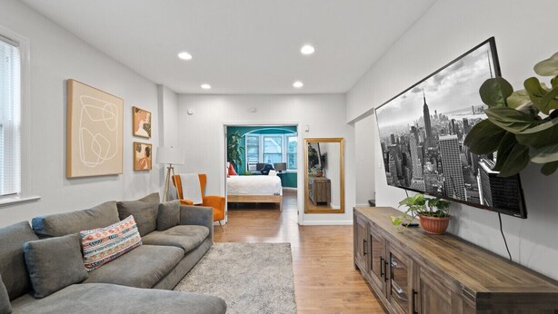 A modern living room with a grey sofa, a flat-screen TV, and a large window.