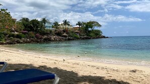 A beach with clear water, a sandy shore, and a row of houses with palm trees.
