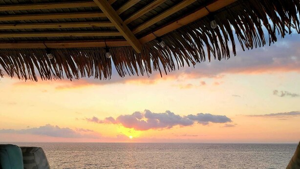 A table with two wine glasses and a bottle, overlooking a sunset over the sea.