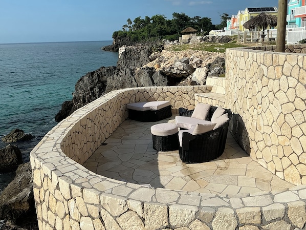 A stone-walled outdoor seating area with wicker furniture, overlooking a rocky coastline and the sea. - Oceanfront, breathtaking views of turquoise Caribbean Sea, gated w/private beach (Negril)