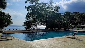 A pool area with clear blue water, surrounded by trees and a view of the sea.