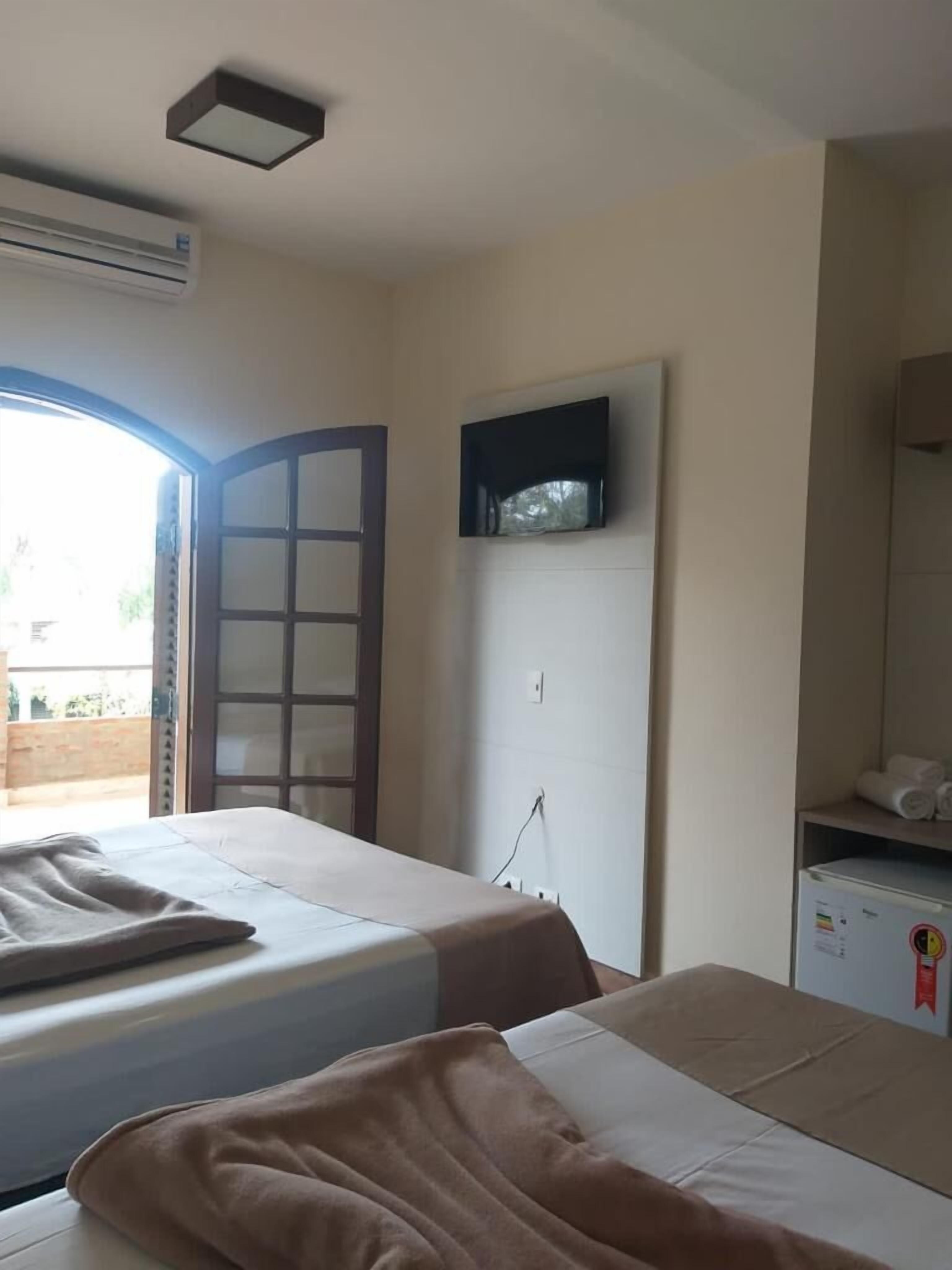 Quarto de hotel com duas camas, televisão na parede, um pequeno frigorífico e janela com vista para o exterior.