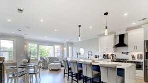 A modern kitchen with white cabinets, a central island with bar stools, and a dining area with a round table and chairs.