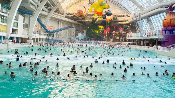 A large indoor swimming pool with multiple lanes, a high ceiling with a glass structure, and various colorful decorations and figures.