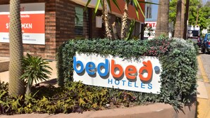 Un letrero de BedBed Hotels con un edificio de ladrillo al fondo.