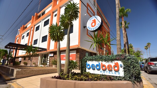 Un hotel llamado 'Bedbed Hotels' con un letrero, palmeras y cielo despejado.