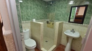 Un baño con inodoro, cabina de ducha y lavabo sobre pedestal.