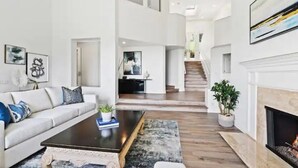 A spacious living area with a sofa, coffee table, and fireplace. A staircase leads to an upper level. - Mansion in La Jolla Heights-Pool, Spa, OceanViews (San Diego)