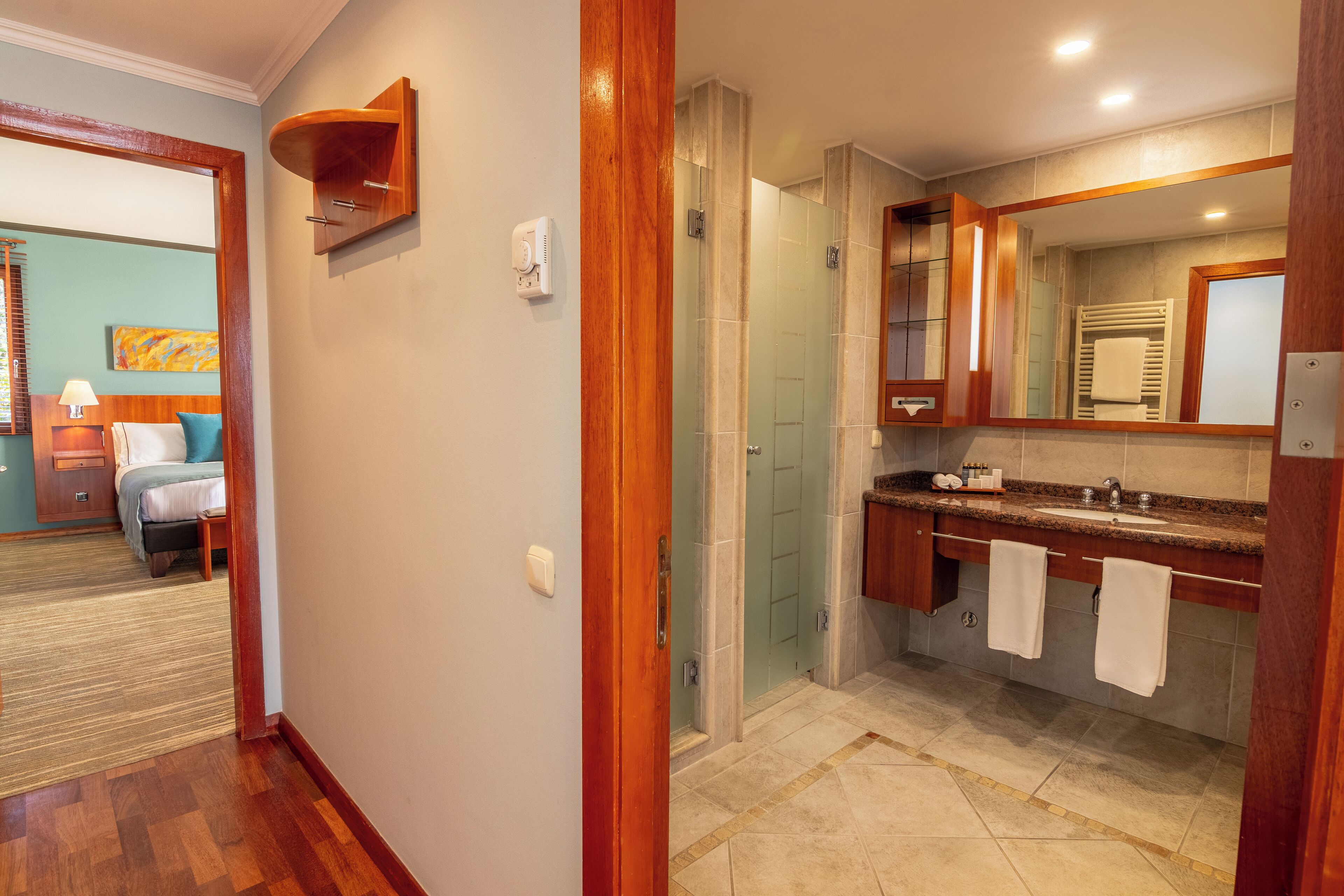 A modern bathroom with a glass shower enclosure, a wooden vanity with a large mirror, and a separate sink area.