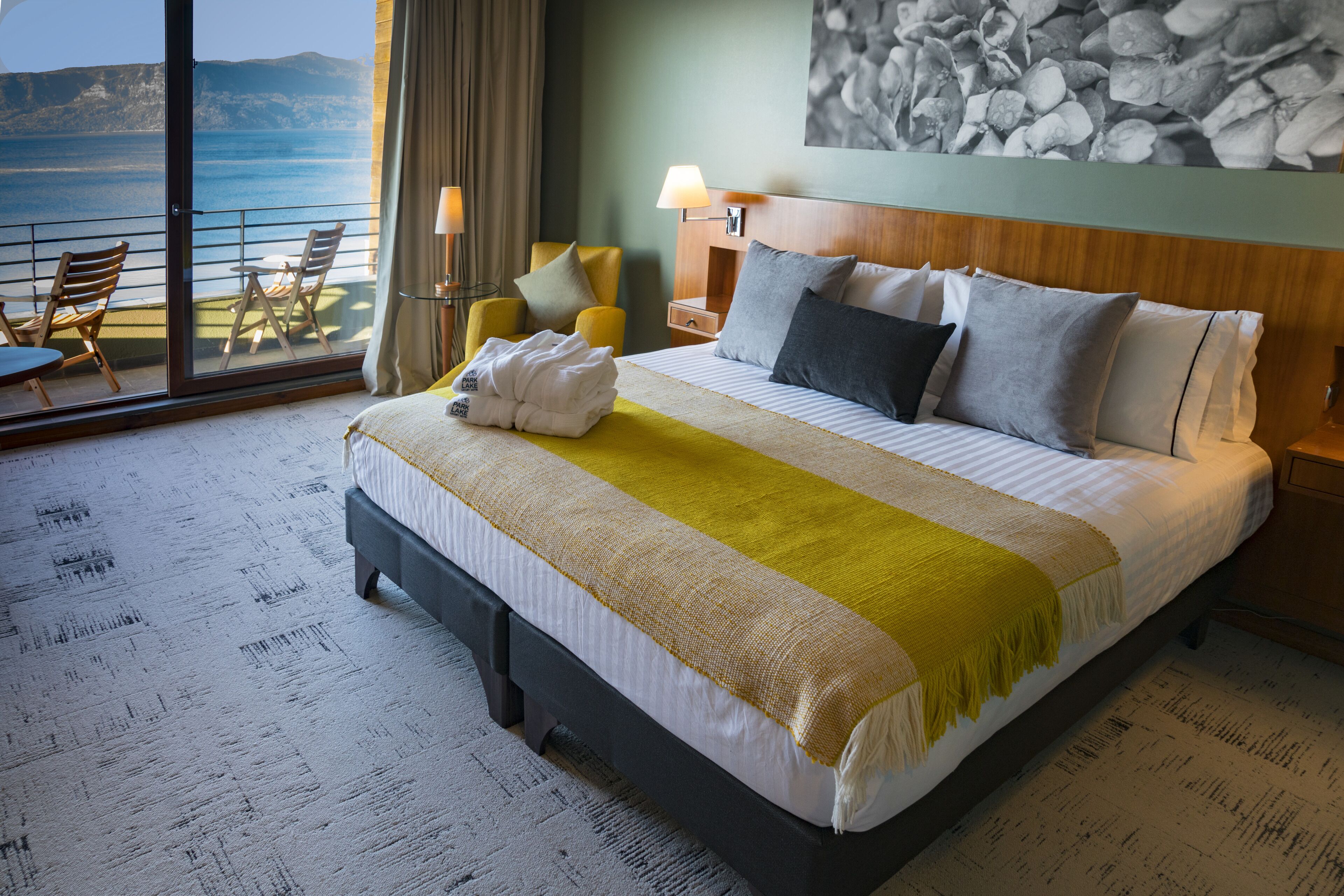 Une chambre d’hôtel avec un lit, une vue sur la mer, un balcon avec des chaises et un tableau au mur.