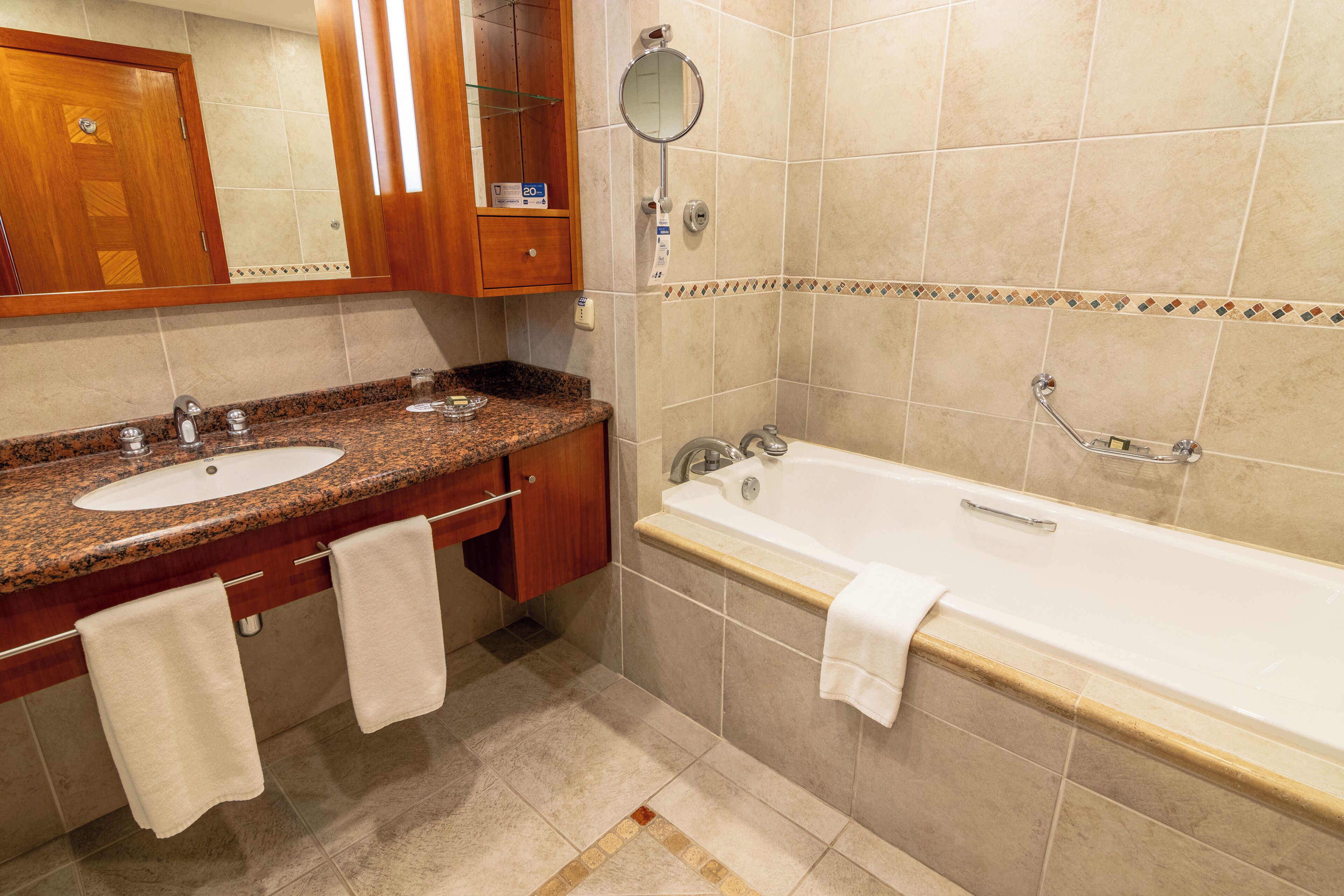 A bathroom with a double sink vanity, a bathtub, and a wooden cabinet with a mirror.