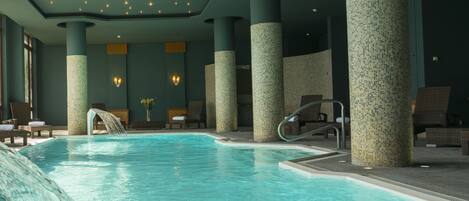 Una piscina interior con tobogán de agua, sillones de descanso y un diseño de columna con azulejos.