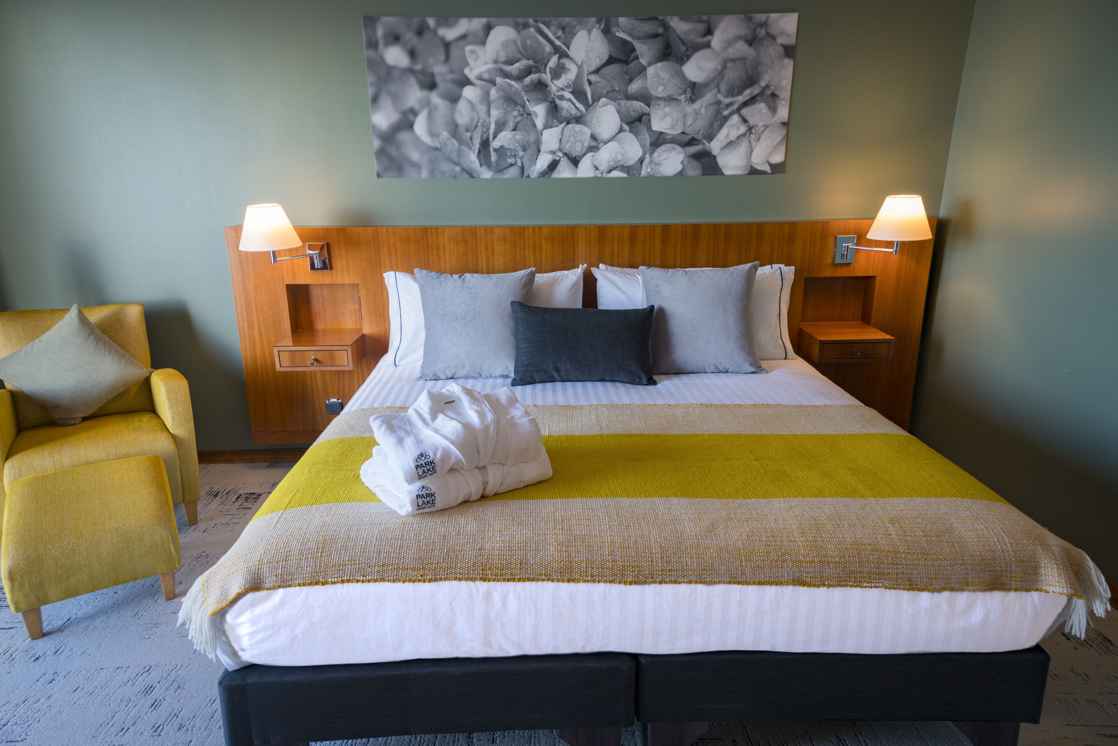 Una habitación de hotel con una cama, dos mesitas de noche, una silla y una obra de arte colgada en la pared.