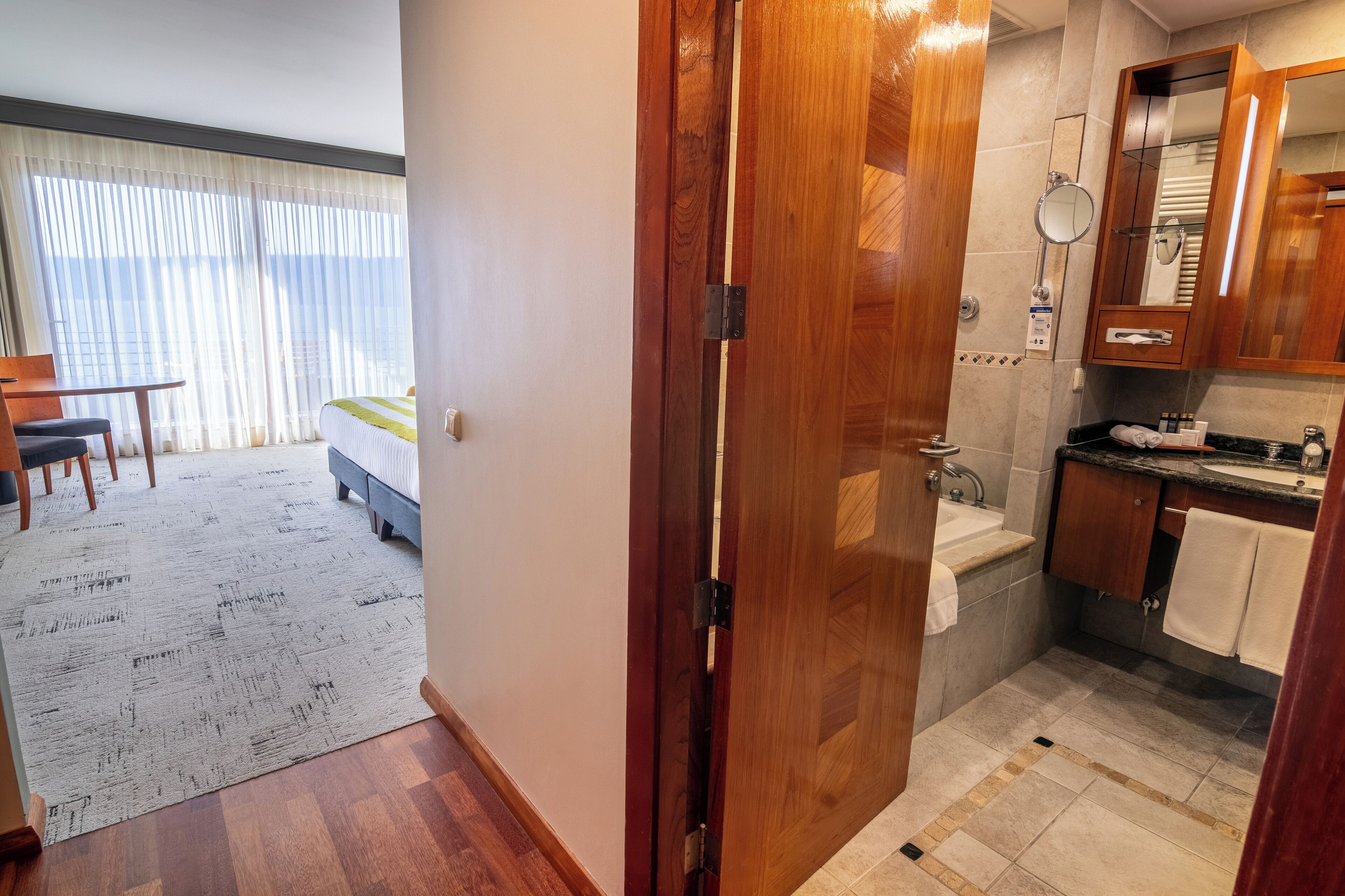 Une chambre d’hôtel comprenant un lit, un bureau, une chaise, une salle de bain avec un lavabo et un miroir, et une vue sur la ville par la fenêtre.