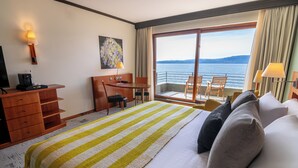 Habitación de hotel con una cama grande, un escritorio, una silla y vista al mar.