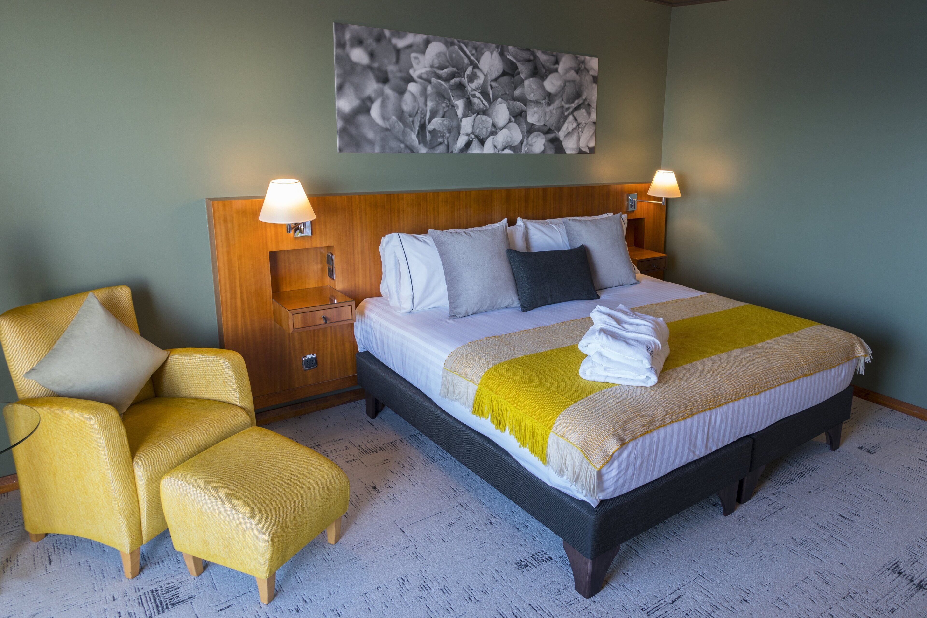 Een hotelkamer met een bed, twee nachtkastjes, een stoel en een klein tafeltje.